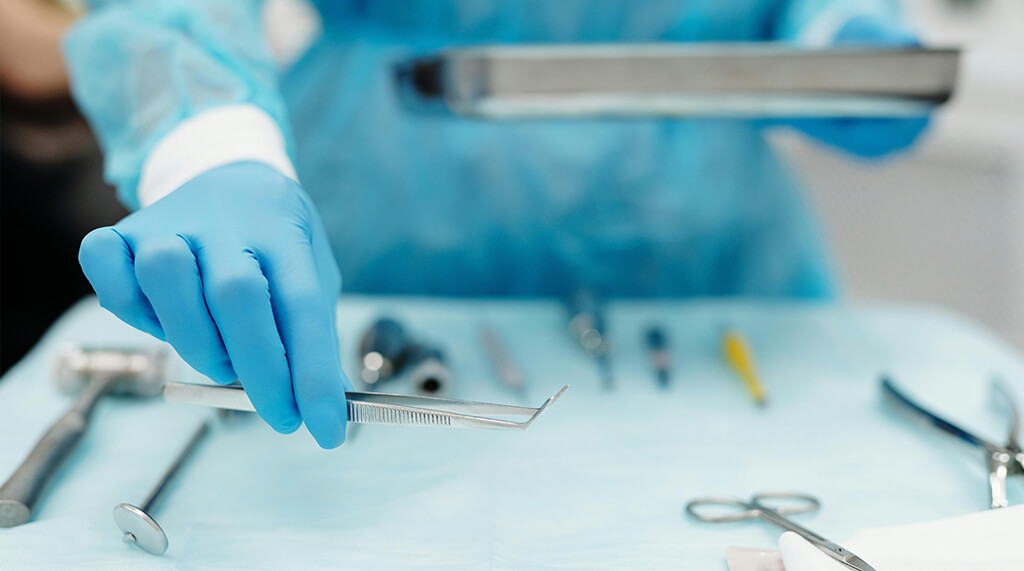 surgical assistant in protective gear and blue gloves arranges surgical tools on table